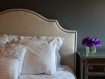 tête de lit cloutée avec oreillers, et table de chevet avec bouquet de fleurs violettes