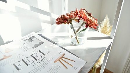 orange flowers in a vase, on a table, next to a magazine