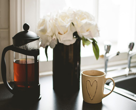 cafetière transparente posé à coté d'un vase de fleurs blanches et d'une tasse